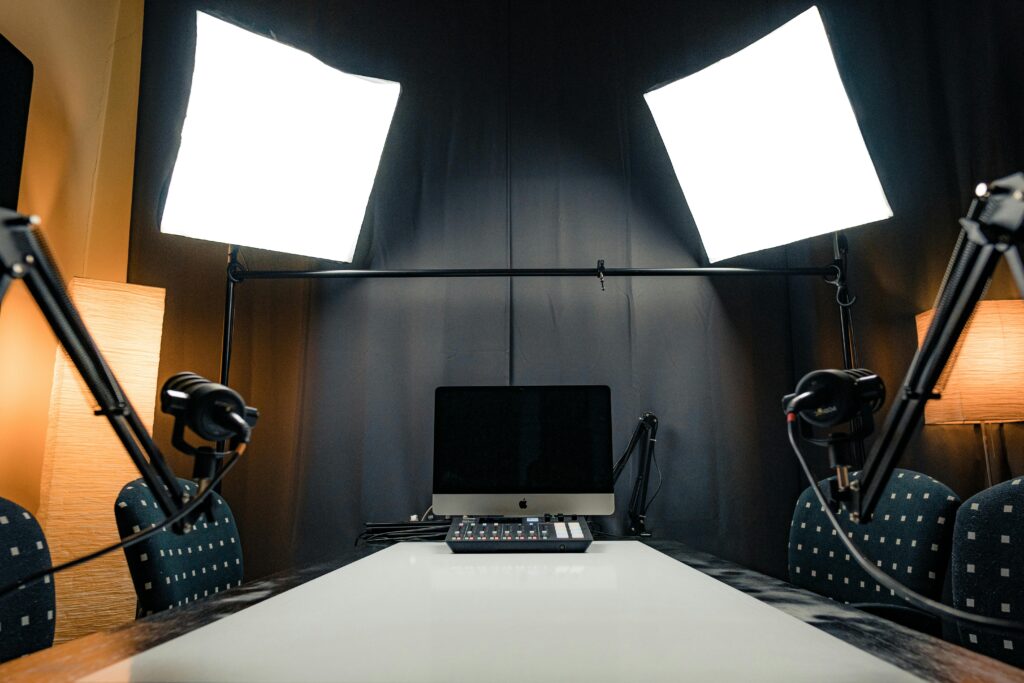 A modern podcast recording studio with microphones, lighting, and computer equipment.